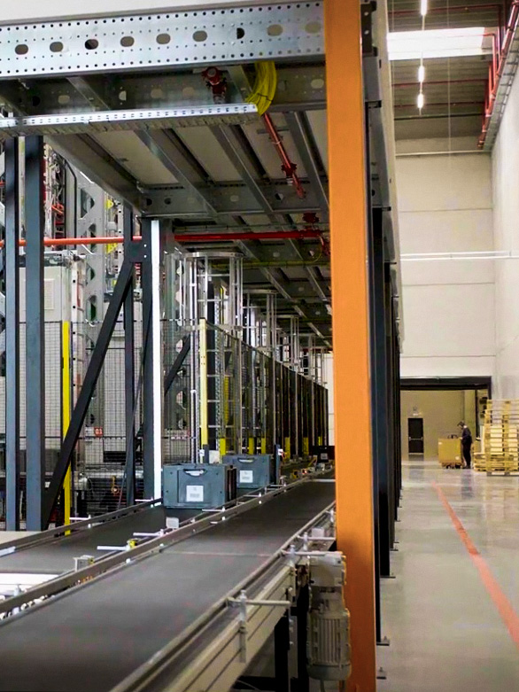 Operatore che attraversa un’area nei pressi di un sistema di trasporto in magazzino, con barriere di sicurezza installate.