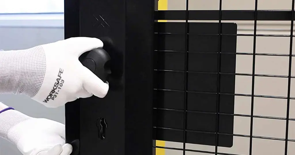 Mano che regge una serratura antipanico a cilindro montata su un pannello a rete nero 