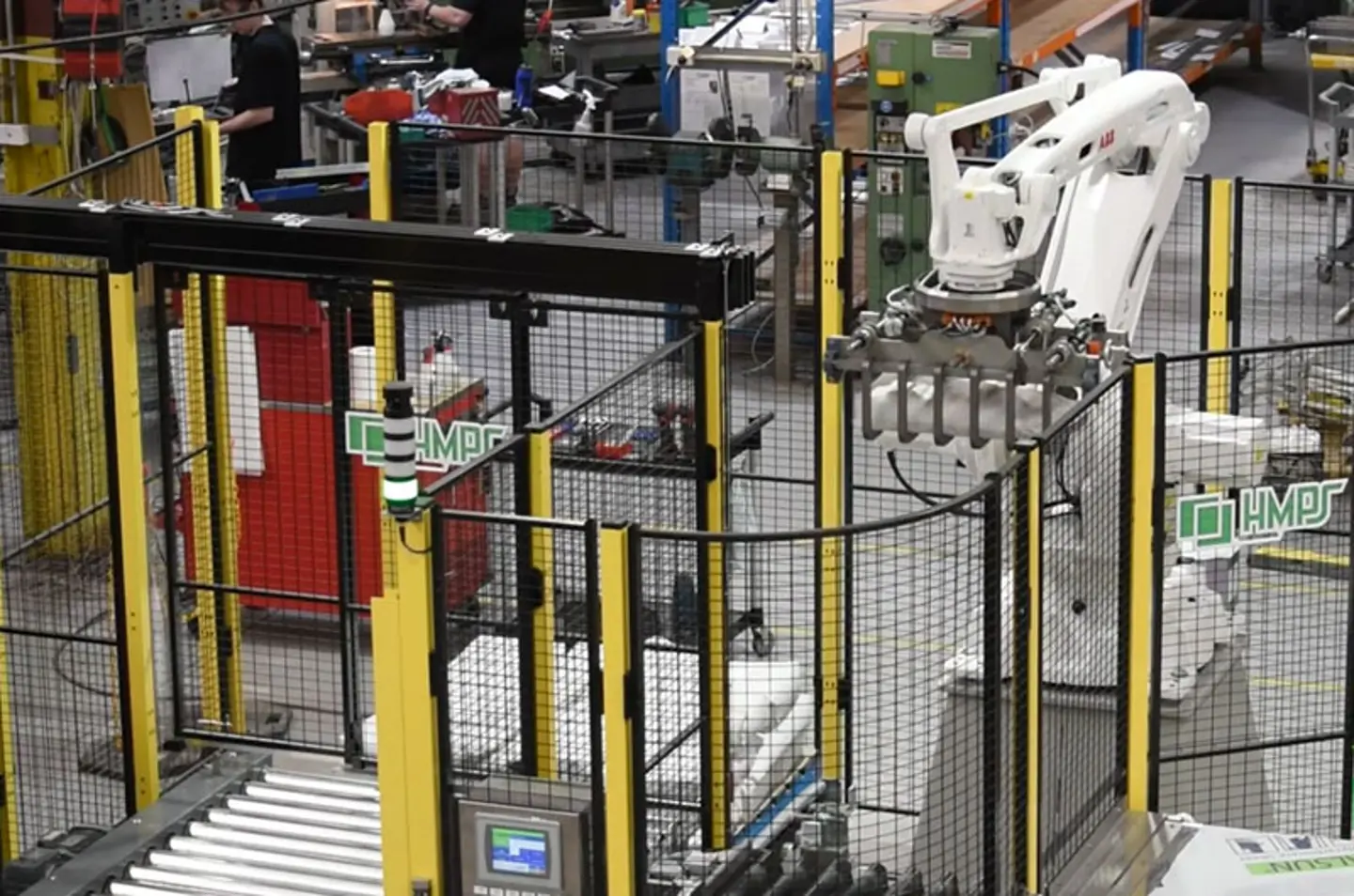 Braccio robotico industriale automatizzato in azione in fabbrica, con sistemi di trasporto a nastro e recinzioni di sicurezza per garantire la protezione degli operatori
