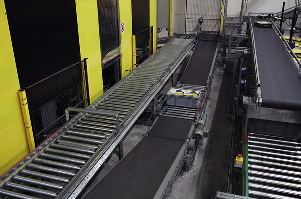 Sistema di smistamento automatizzato in magazzino con nastri trasportatori e recinzioni di sicurezza per la logistica ad alta velocità.